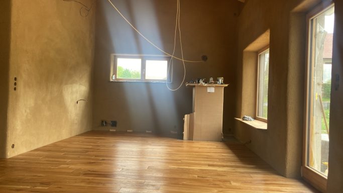 Lichtdurchfluteter Neubau-Raum mit warmem Holzboden und Lehmputz – die perfekte Basis für ein natürliches, modernes Zuhause.