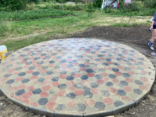 Rundes hexagonales Pflaster aus rot-grau Beige Betonziegeln auf frischem Gartengrund – modern und robust. 